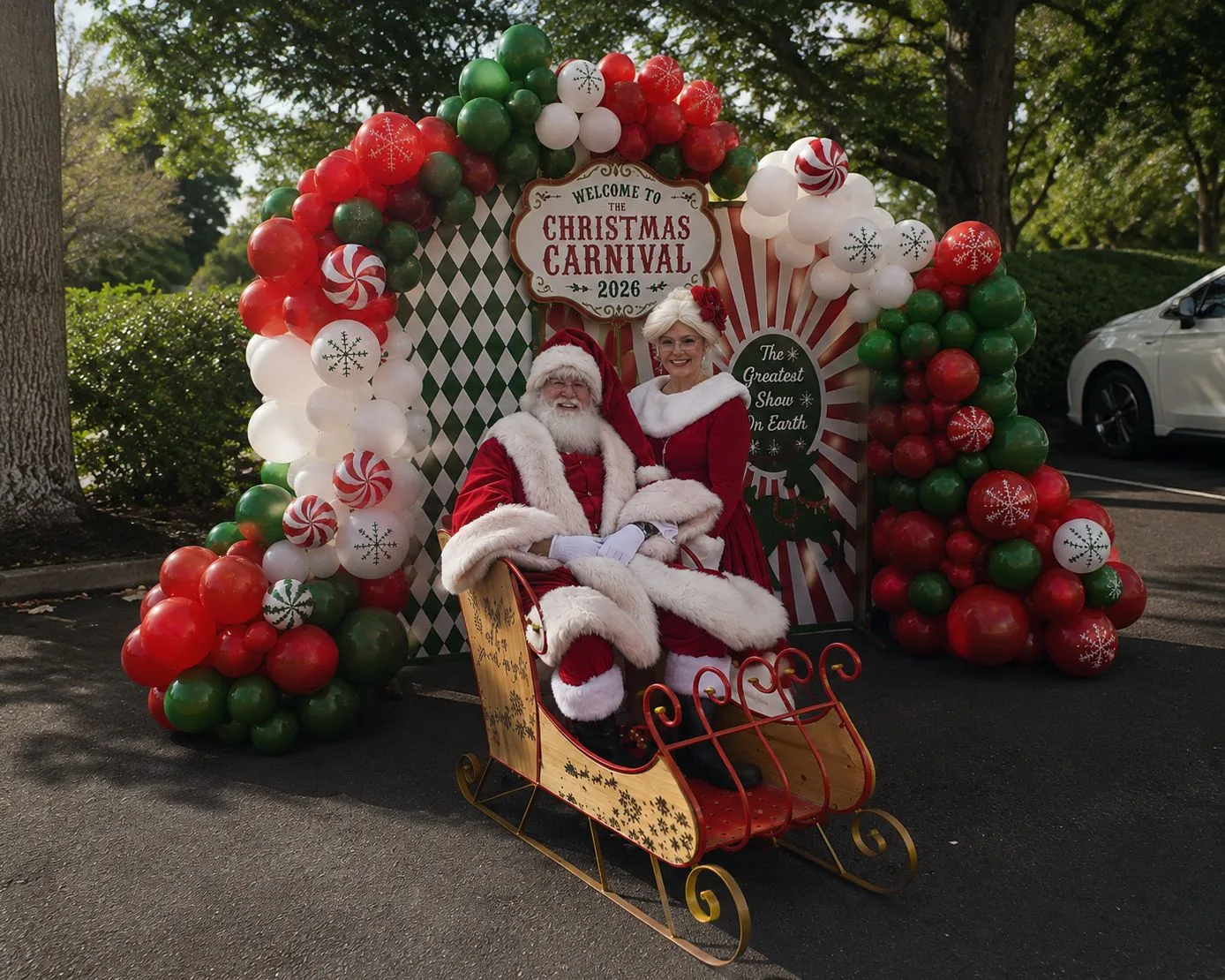 Santa and Mrs. Claus posing under a red-and-white balloon arch flanked by gingerbread figures, with palm trees in the background