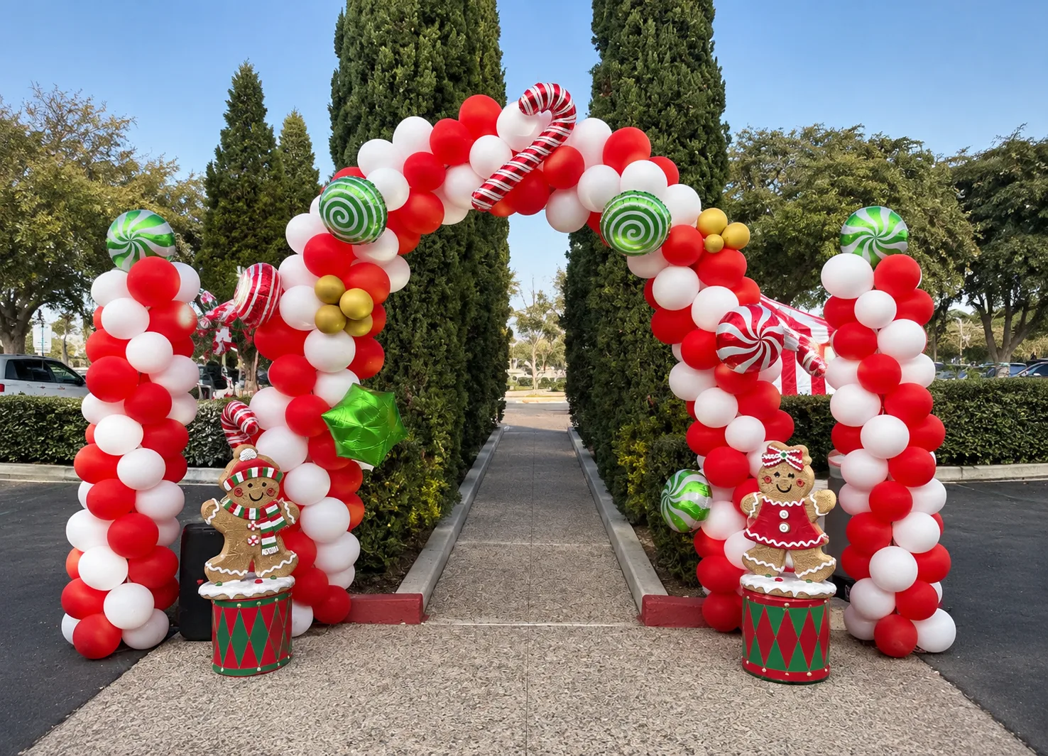 A red-and-white balloon arch trimmed with candy canes, peppermint balloons, and gingerbread figures on toy drums, in daylight